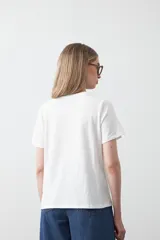 Remera blanca de algodón de manga corta, con cuello redondo y bordado frontal en hilo color beige claro con la palabra "J'adore" en tipografía cursiva.