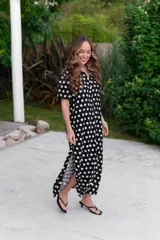 Camisola negra con estampado de lunares blancos, cuello camisero y mangas cortas. Tiene corte recto y largo midi con aberturas laterales.