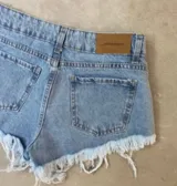 Short de jean celeste con efecto lavado, tiro alto, bolsillos delanteros y traseros, cierre con botón y cremallera. Detalle de flecos en el ruedo.