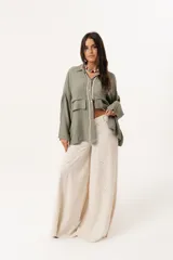 Camisa verde militar de manga larga con silueta oversize, dos bolsillos delanteros y corte levemente más largo en la espalda. Escote en V abotonado con detalle de galón picot a lo largo de la cartera y botones a tono. Isotipo bordado en la parte trasera.