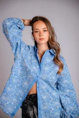 Camisa celeste con estampado de flores blancas, corte clásico, cuello camisero y mangas largas abullonadas.