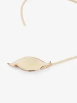 Collar rígido asimétrico color dorado, con dije en forma de hoja metálica lacada en color crema.