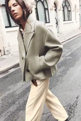 Abrigo corto color verde oliva, de cuello solapa y manga larga. Cuenta con bolsillos delanteros de vivo y cierre frontal cruzado con botones.