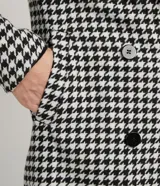 Campera alargada con cuello solapa, bolsillos y cierre de doble abotonado. Presenta un estampado cuadrillé pied-de-poule en blanco y negro, con un detalle contrastante en el puño. Confeccionada en polivelour, con forro de poliéster.