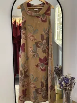 Vestido midi color camel con estampado de flores en tonos borgoña, marrón y verde, de lino italiano, corte acampanado y cuello caído.