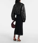 Campera bomber corta de cuero sintético negro, con cuello alto, cierre frontal, hombreras con botones a presión y bolsillos con solapa y botón a presión.