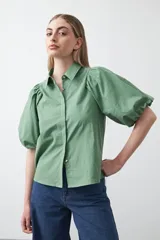 Camisa de algodón color verde salvia, con cuello camisero, botones frontales y mangas cortas abullonadas con elástico en el puño.