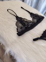 Conjunto de lencería negro de encaje, compuesto por un bralette con breteles regulables y una tanga regulable con corte cola less y entrepierna de algodón.