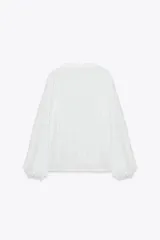 Blusa blanca de manga larga con escote en pico, detalle de tejido con frunces, entredoses y plumeti. Cierre frontal con botones.