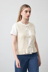 Chaleco tejido de punto color beige con trama texturada y diseño liviano. Presenta cuello a la base, silueta recta y cierre frontal mediante tres lazos delicados.