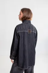 Camisa de denim azul oscuro, con cuello, bolsillos frontales con tapa y bordados en rojo en el bolsillo derecho. Presenta un calce holgado y mangas largas.