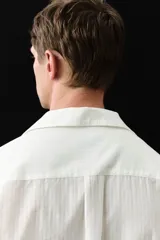 Camisa blanca de manga larga en mezcla de lyocell y algodón. Corte estándar, cuello inglés, tapeta clásica, bolsillo superior abierto, canesú con pliegue de caja en la espalda y bajo redondeado.