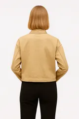Campera corta color beige, de corte holgado, con cuello alto, cierre frontal con cremallera, bolsillos con solapa y cordón ajustable en el ruedo.