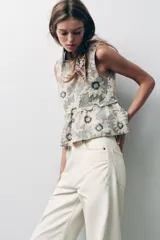 Top sin mangas con estampado de flores blancas y negras, cuello redondo, corte peplum y cierre con botón en la espalda.