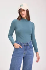 Blusa de punto canalé color verde azulado, de cuello alto y manga larga.