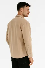 Sobrecamisa beige de corte recto, con cuello camisero, cierre frontal con botones a tono, mangas largas con puños abotonados, dos bolsillos de parche en el pecho y ruedo recto.