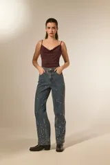 Pantalón jean color natural de calce alto y corte recto, con bolsillos y detalles de strass dispersos por las piernas.
