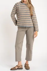 Sweater de tejido de punto con diseño de rayas horizontales alternando gris y beige. Presenta cuello redondo y mangas largas con costura decorativa visible en los laterales.