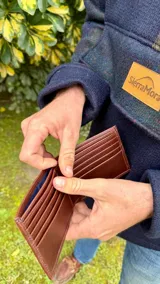 Billetera de cuero marrón con costuras a tono y múltiples compartimentos para tarjetas y billetes.