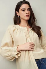 Camisa color crema de lino con cuello redondo, canesú fruncido, mangas largas amplias con puños elastizados con volado y cierre frontal con botones.