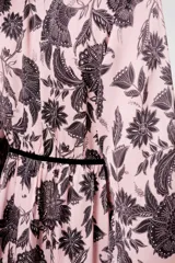 Vestido largo rosado con estampado floral negro, escote en V con ribete negro, mangas largas abullonadas y falda escalonada con volantes.
