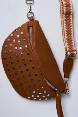 Riñonera color camel con tachas plateadas y correa de tela con diseño geométrico en tonos beige y blanco.