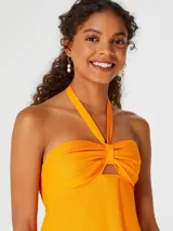 Vestido largo naranja con escote halter y detalle de nudo en el pecho.