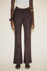 Pantalón marrón acampanado de tiro alto confeccionado en tejido efecto ante con detalle de tachas en la cintura.