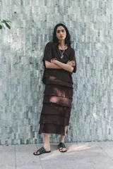 Vestido midi color marrón oscuro confeccionado en hilatura con viscosa y algodón. Tiene cuello redondo, manga corta y bajo con volantes desflecados y aberturas laterales.