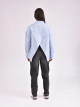 Camisa celeste de corte amplio, con cuello clásico, cierre frontal con botones, bolsillo en el pecho y mangas largas con detalle de botones en los puños.