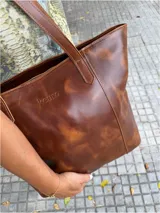 Bolso tote de cuero color dorado con textura de piel de cocodrilo. Tiene doble asa de hombro, cierre superior, bolsillo interior y llavero.