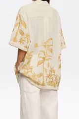 Camisa color crema con bordado de hojas color mostaza, de corte recto, manga corta y cuello camisero.