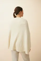 Poncho color crema de tejido de punto industrial con cuello alto y aberturas laterales para los brazos.