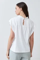 Blusa blanca de algodón con cuello redondo fruncido y mangas cortas con volados.