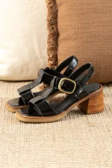 Sandalias negras de charol con tiras entrecruzadas, hebilla dorada y tacón de madera.