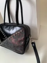Cartera rígida artesanal de cuero negro con tachas plateadas, herrajes y cierre metálico plateado marca YKK. Tiene asa fina para llevar al hombro o en la mano y correa larga extra regulable. El interior es forrado, con un bolsillo con cierre enmarcado en cuero y un segundo bolsillo plaqué.