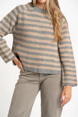 Sweater de tejido de punto con diseño de rayas horizontales alternando gris y beige. Presenta cuello redondo y mangas largas con costura decorativa visible en los laterales.
