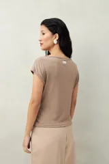 Top color beige de tejido acanalado, con cuello recto, sin mangas y terminación asimétrica en pico.