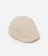 Boina color beige confeccionada en sarga de algodón, con botón en la parte superior y cierre de elástico.