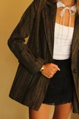 Blazer negro con rayas verticales en hilo dorado brillante, con solapas y un botón frontal.