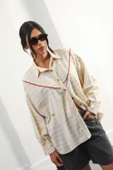 Camisa color crudo a rayas, de corte oversized con hombros caídos y silueta amplia. Presenta un recorte delantero con vivo contrastante, botones al frente y logo bordado al frente.