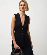 Chaleco negro de tejido punto, sin mangas, con cuello solapa y cierre frontal de dos botones dorados. El corte es acinturado y alargado.