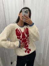 Sweater tejido a mano en Uruguay, confeccionado en lana merino color crudo, con diseño de langosta roja en el frente y detalles en azul en cuello y puños.
