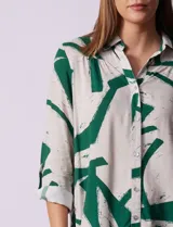 Camisa de manga larga con estampado abstracto en tonos verde y blanco. Cuello con solapa y abertura central con botones. Largo de manga regulable con presilla y botón. Terminación de ruedo anudada opcional.