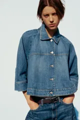 Cazadora de denim azul de corte holgado, con cuello solapa y manga tres cuartos acabada en puño. Cierre frontal con botones metálicos.