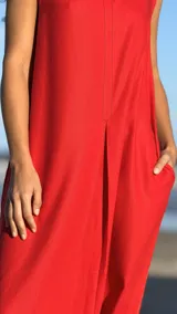 Vestido largo rojo sin mangas, de lino con pespuntes en tono más oscuro y pinzas. Tiene cuello redondo y bolsillos laterales.