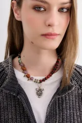 Gargantilla corta con cuentas de diferentes colores y texturas, separadas por piezas metálicas doradas y plateadas. Incluye dije central con forma de escudo plateado.