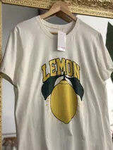 Remerón blanco de algodón con estampa de un limón con hojas y la palabra "LEMON" en amarillo y negro.
