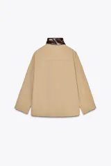 Cazadora color beige con cuello alto en tejido efecto piel marrón a contraste. Manga larga, bolsillos delanteros, detalle de pespuntes a tono, forro interior y cierre frontal con cremallera y botones a presión ocultos por solapa.