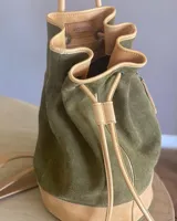 Bucket bag de gamuza, con bolsillo exterior e interior con cierre, correa ajustable y mango firme para usar como bolso de mano.